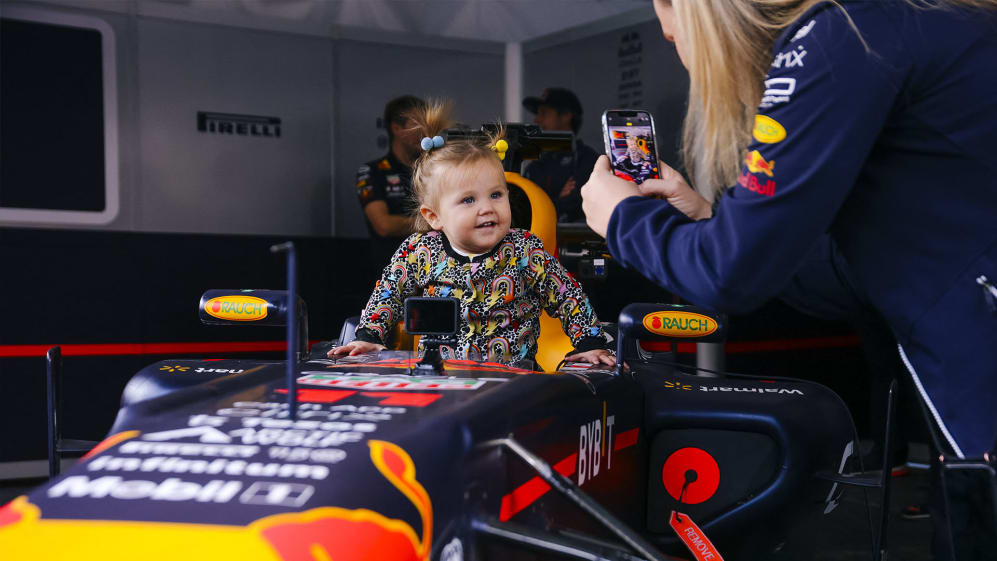 A LITTLE GIRL POSING FOR A SNAPSHOT IN REDBULL F1 CAR 